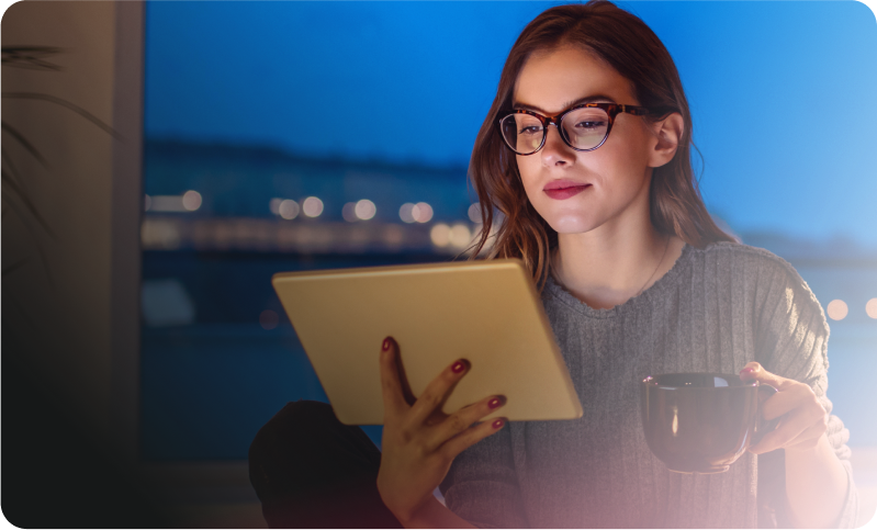 imagem de uma mulher de óculos segurando uma xícara na mão esquerda, segurando um tablet com a mão direita e olhando fixamente para ele